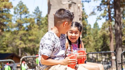 Two kids smiling at each other holding a drink outdoors in the summer