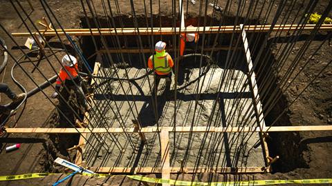 Construction workers on dirt with metal and wood features surrounding.