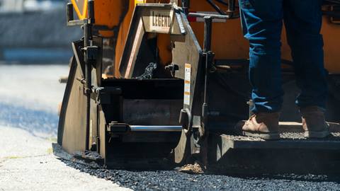Adult on asphalt paver laying down new asphalt in Snow Valley parking lot.