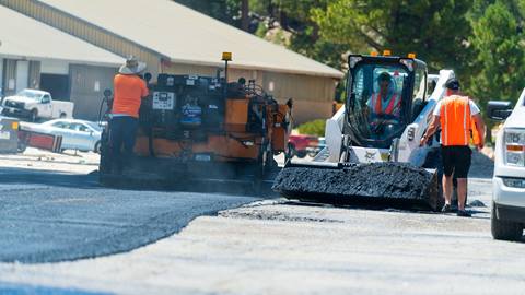Construction workers laying down black asphalt for paver to roll over and flatten out.