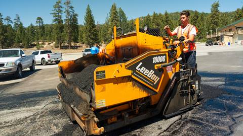 Adult construction worker in parking lot near cars on asphalt paver.