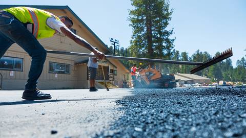 Adult raking out asphalt in Snow Valley parking lot.