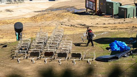 Two adults in black apparel carrying a white chairlift to lay on the dirt next to over 15 other chairlifts during a chairlift overhaul project.