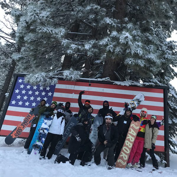 Group of snowboarders taking a photo in front of a wooden american flag in the snow
