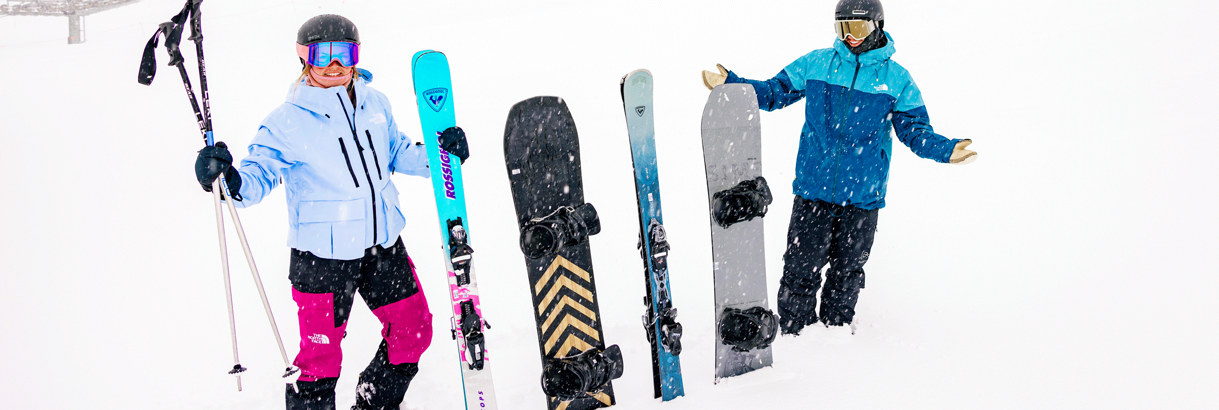 Two riders holding up ski and snowboarder gear in the snow on a snowy day at Big Bear Mountain Resort