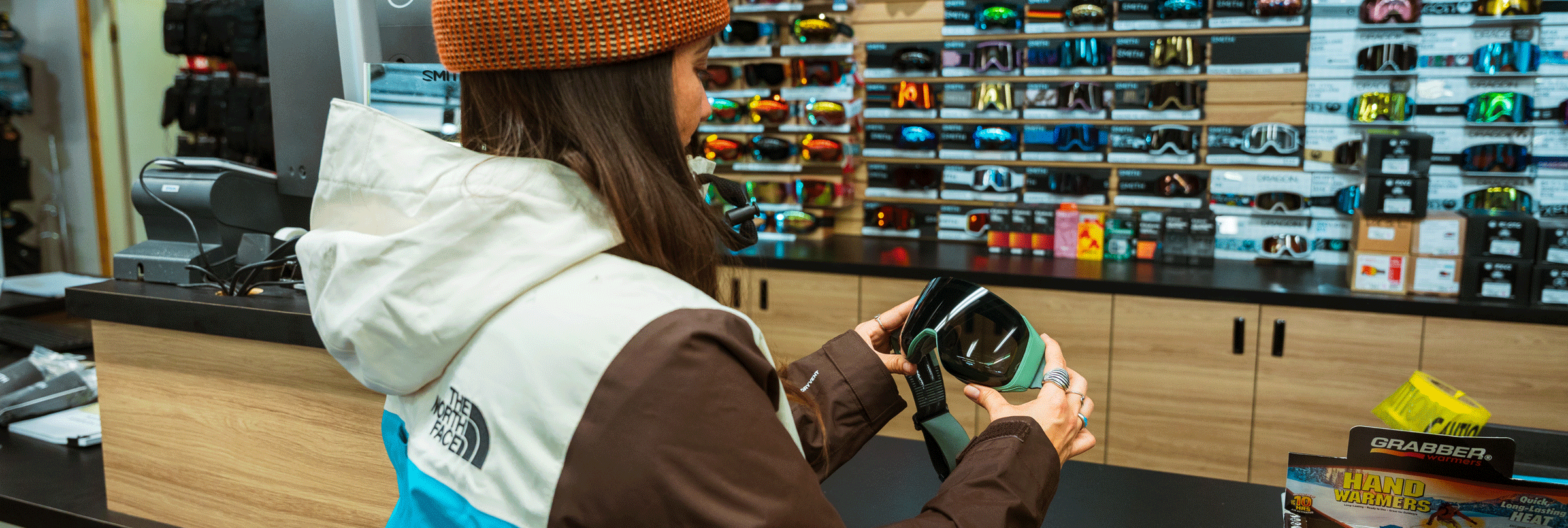 female snowboarder looking at snow goggles in the Snow Valley sports shop