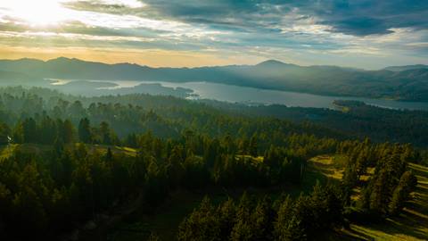 A scenic drone shot over Snow Summit during a summer evening with the forest trees and Big Bear Lake in the distance as the sun sets.