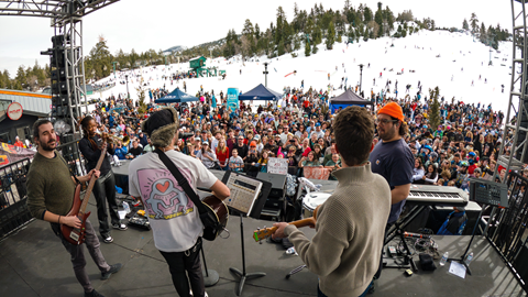 Backstage view of a band playing with a large crowd in front of the snow and ski slope at Bear Mountain