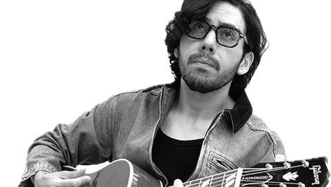 Adult with glasses and a beard playing a guitar.