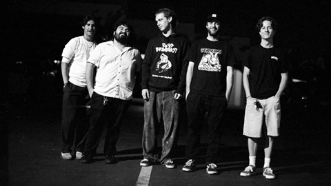 A black and white group portrait of the five members of the Dogs Breakfast band standing together and posing for the camera.