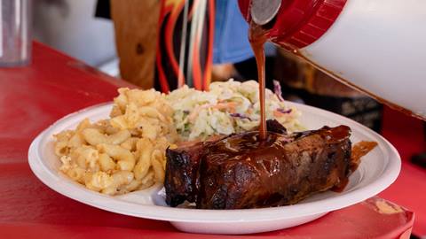 A plate with BBQ meat, coleslaw, and macaroni with sauce being poured over the meat.