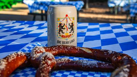 A big pretzel and a Big Bear Lake beer stein laying on a table with blue and white checkerboard pattern tablecloth.