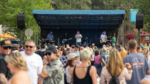 A large crowd gathered outside during a summer concert series event with a band playing on a stage.