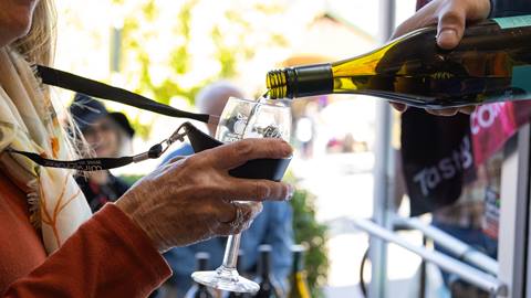 Adult holding up a wine glass that has another adult pouring wine into it.