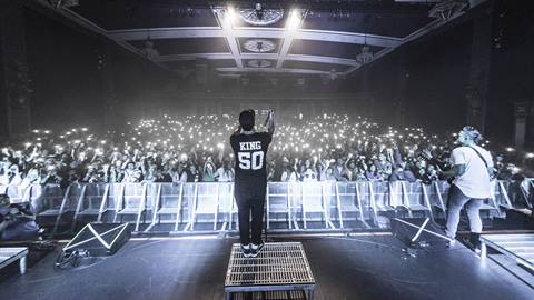Common Kings band performing on stage in front of a large audience with their phone flash lights lighting up the crowd.