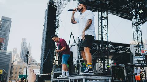 Two members of Common Kings, standing on platforms on the stage, singing and playing guitar to a crowd.
