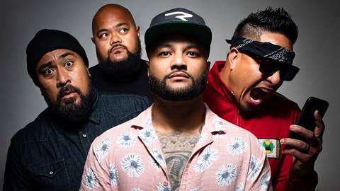 Up close group shot of the four band members of the reggae group, Common Kings. From left to right: adult in black shirt and black beanie, bald headed adult in black shirt looking up, adult in black hat with light pink flower button up showing tattoos on chest, and on the right an adult wearing a black bandana and red shirt yelling at their phone.