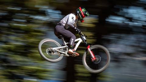 A mountain bike rider, mid-air on their white frame bike, wearing blank pants, a white jersey, full face helmet with red goggles.
