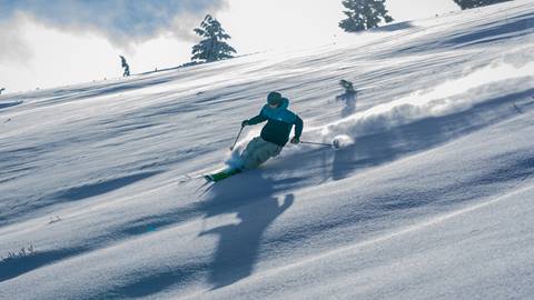 A skier in blue jacket skiing down an untouched powdery trail on a sunny day at Snow Valley.