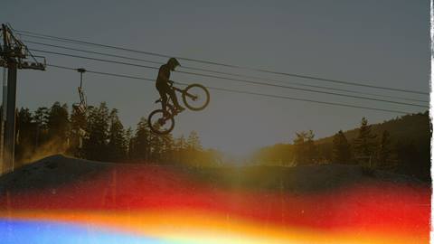 Mountain biker doing a jump off a little dirt ramp with the chairlift cables in the background