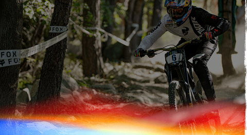 A mountain biker wearing a full-face helmet and protective gear riding down a dirt trail through a forested area.
