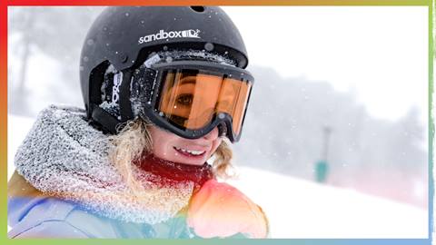 Adult smiling on the slopes in a helmet and goggles while snow is falling