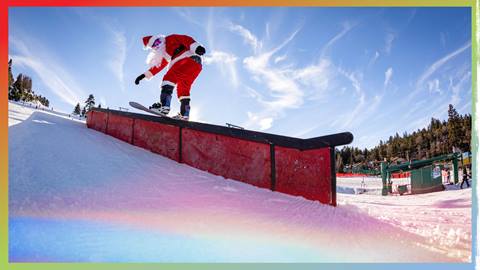 A Santa snowboarder front board sliding a terrain park rail feature at Bear Mountain