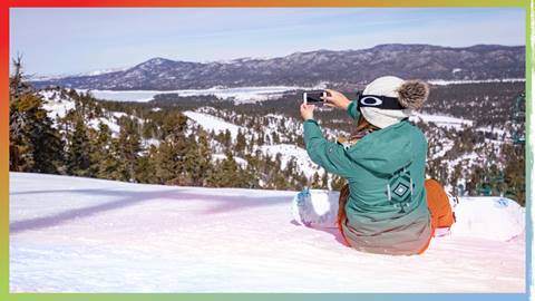 Snowboarder sitting on slopes taking a picture of the views