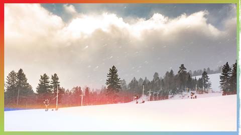 A stormy day at Snow Summit with light snow falling onto a snowy winter trail and the sun peaking through clouds in the sky.