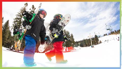 two kiddos with snowboards walking on snow