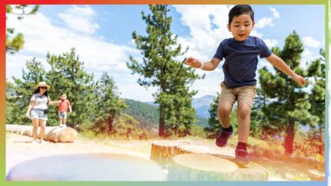 Kiddo on a tree stump with family in the background
