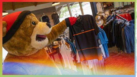Biggie the mascot holding up an Oakley golf shirt in the Bear Mountain Golf Course Pro Shop