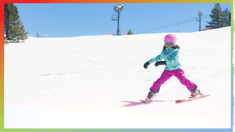 Child on skis going downhill, wearing pink snow pants and helmet, and a teal snow jacket