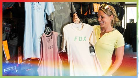 female shopper holding up a fox head branded tan tshirt, looking at it, smiling