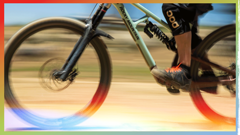 Close-up side profile of a person riding a mountain bike at high speed, with a colorful, warm motion blur in the background.