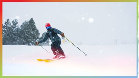 A skier in all black with a red helmet skiing down a ski trail on a cloudy snow storm day.