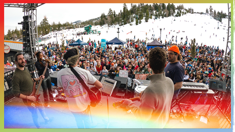A band playing live on a stage at bear mountain with a crowd and snow in the background