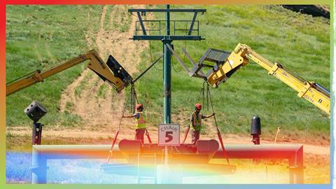 Two employees in red hard hats and yellow with orange vests assist two forklifts with a chair five chairlift project during summer at the base of Bear Mountain.