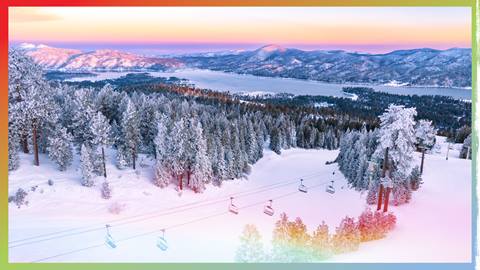 Morning sunrise over Snow Summit with fresh snow on the trees and trails, Big Bear Lake in the distance, and a pink to orange to blue gradient glow in the sky.