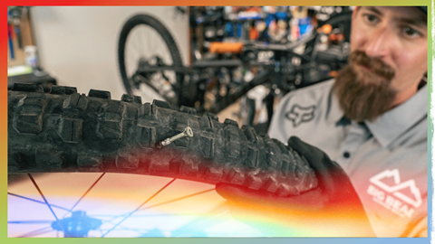 Bike technician looking at a bike wheel that has a nail in it, this image has a rainbow overlay on it