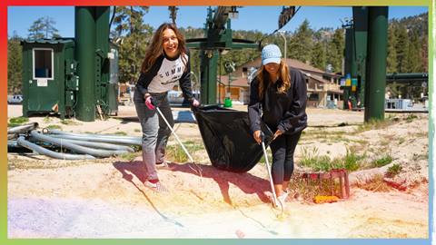 Two adults at the base of Snow Valley in front of a chair lift picking up trash during a staff clean up day.