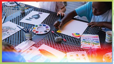 A close-up of a child painting with colorful watercolor palettes during an outdoor summer youth activity at Biggie's Adventure Outpost at Big Bear Mountain Resort.