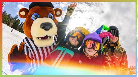 Big Bear Mountain Resort mascot, Biggie, on the snow at Bear Mountain doing a photo opportunity with three excited kiddos wearing snow helmets, goggles, and jackets on a partially sunny day.