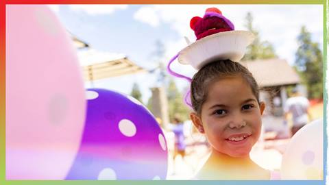 A kiddo next to balloons with a birthday hat on their head