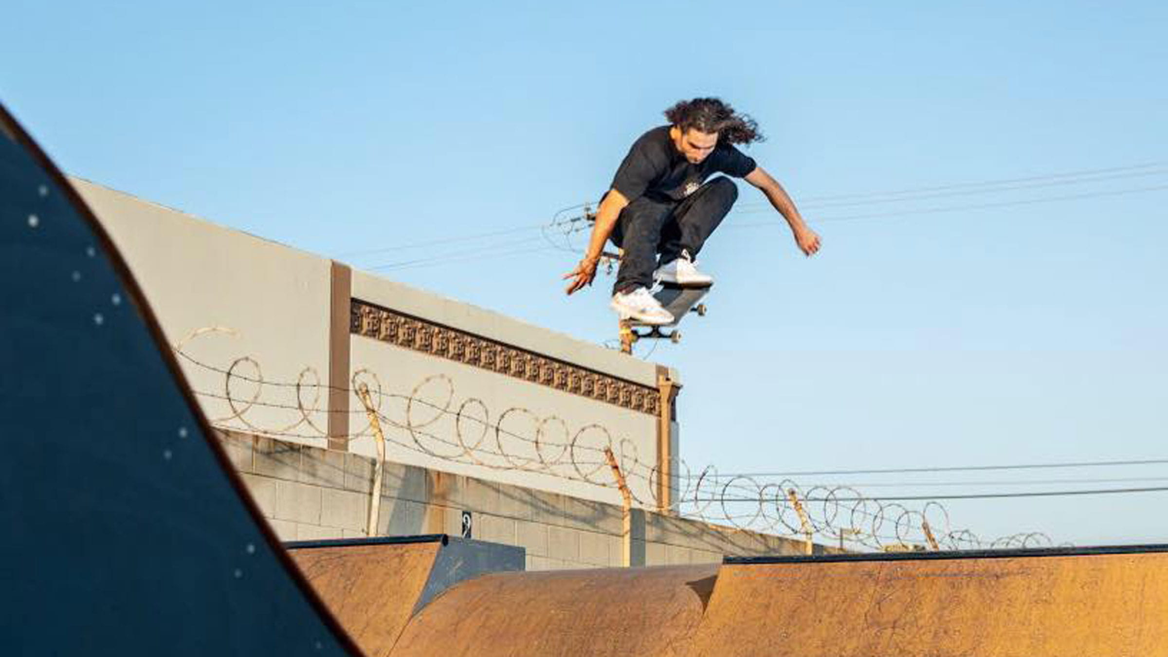 Pro skater, Mike Berdis, in black shirt and dark pants getting air out of a wood halfpipe on a blue sky day.