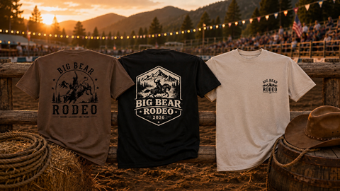 A army green, black, and white t-shirt with Big Bear Rodeo logos and designs displayed against a mountain sunset.
