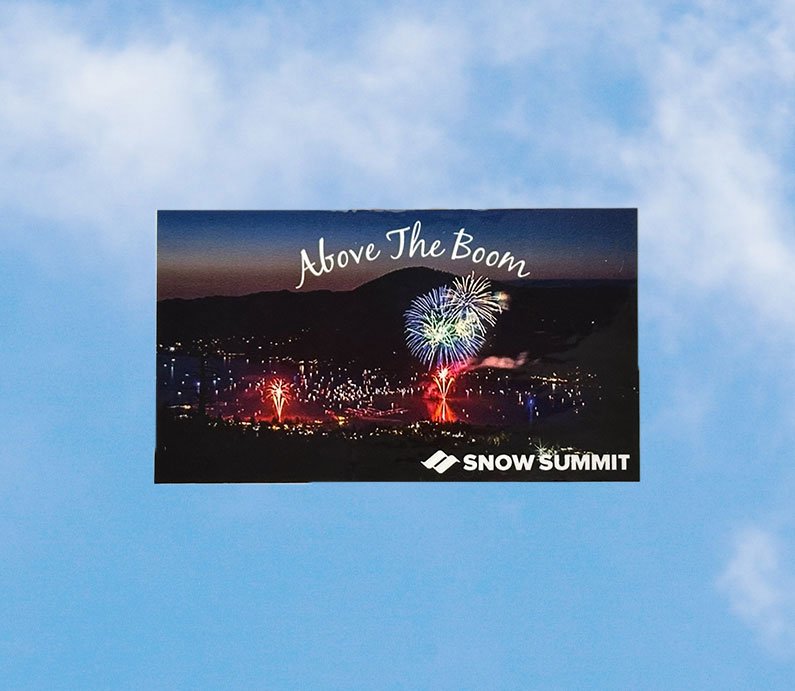 Above the Boom sticker of Big Bear Lake's annual 4th of July firework spectacular, Above the Boom, with an arial view of fireworks in the sky over the lake. On the bottom right corner, white Snow Summit logo.