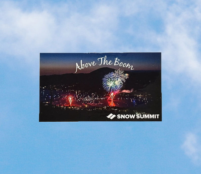 Above the Boom sticker of Big Bear Lake's annual 4th of July firework spectacular, Above the Boom, with an arial view of fireworks in the sky over the lake. On the bottom right corner, white Snow Summit logo.