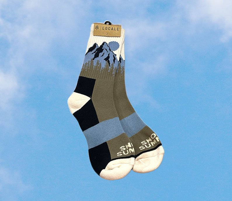 Blue, forest green, black, and white Locale Snow Summit sock with mountain forest design.
