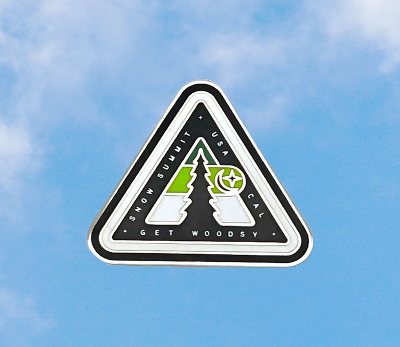 Snow Summit woodsy logo on a pin with green coloring and a pine tree with star and crescent moon symbol.